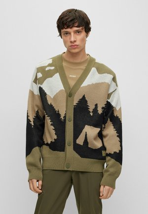 Green knitted cardigan with mountain and forest pattern, featuring a v-neck, button front, and textured surface. Accented with black and beige.