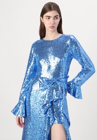 Plava haljina s kićankama, dugim rukavima, okruglim izrezom i prorezom do butina. Glatka tekstura; sjajna površina.
