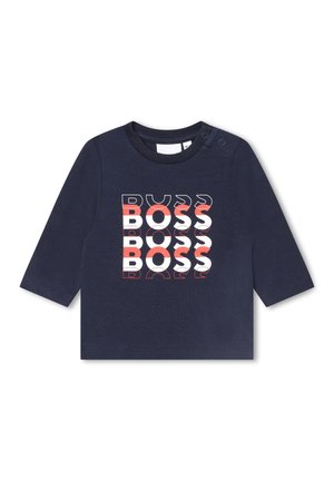 Chemise à manches longues bleu marine pour tout-petit avec le mot "BOSS" répété trois fois en texte blanc et rouge sur le devant, et des boutons-pression sur une épaule.