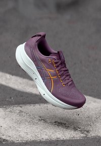 Purpura sporta apavi ar fakturētu augšdaļu, baltu vidusdaļu un oranžiem un ziliem akcentiem. Iespējo lacing sistēma un mīkstināta zole.