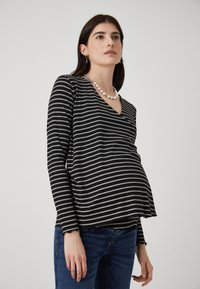 Schwarz-weiß gestreiftes Langarmshirt mit V-Ausschnitt, lockerer Passform und weichem Material, kombiniert mit blauen Jeans.