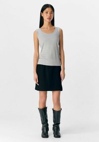 Grijze mouwloze tanktop met een ronde halslijn, gecombineerd met een zwarte rok tot de knie en zwarte kniehoge laarzen. Glad materiaal en een strak design.