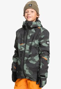 Camouflagejacka i nyanser av mörkgrön och svart med orange accenter, med dragkedjestängning, huva och justerbara ärmslut.