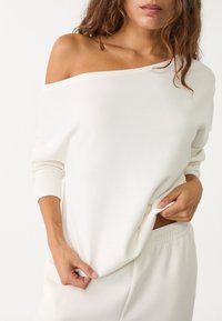 Sweat-shirt écru à épaules dénudées avec manches longues et poignets côtelés, en tissu doux, coupe légèrement ample.