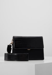 Borsa nera con texture a stampa coccodrillo, chiusura a pattina e tracolla staccabile. Gli accessori in oro esaltano il design.