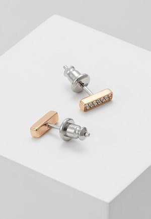 Obdélníkové náušnice s pozlaceným tónem a řadou malých průhledných krystalů, vystavené na bílém povrchu.