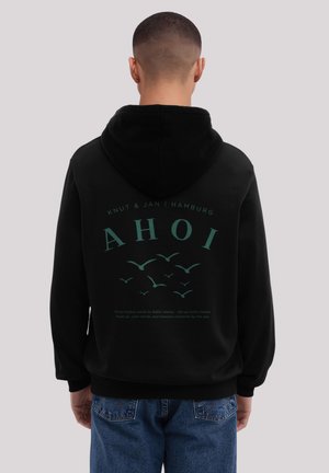 Schwarzer Hoodie mit einer vorderen Kängurutasche und grünem Grafikdesign auf der Rückseite, das den Text "AHOI" und fliegende Vögel zeigt. Der Text enthält zusätzliche Details.