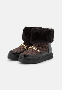 Zwarte en bruin gemêleerde enkellaarzen met een bontkraag, glanzende lakleren accenten en een gouden kettingdetail aan de voorkant.
