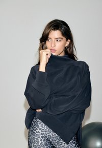 Sort oversized sweatshirt med høj krave og glat tekstur. Kombineret med grå leggings med leopardprint, der viser et tætsiddende design og elastisk materiale.