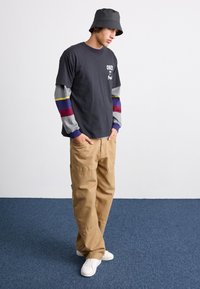Black graphic T-shirt with "OBEY" text, layered over multicolored long sleeves; beige cargo pants and white sneakers complete the outfit.