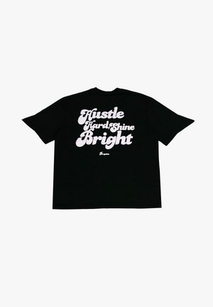 Sort bomulds t-shirt med fed hvid tekst: "Hustle Hard, Shine Bright." Oversize pasform med korte ærmer og rund hals.