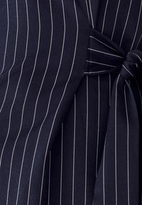 Tejido azul marino con rayas blancas, que presenta un detalle de nudo atado. Textura suave con un diseño ajustado, que enfatiza líneas estructuradas.