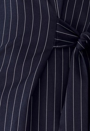 Námornícka tkanina s bielymi pruhmi, so zaviazaným uzlom ako detail. Hladká textúra s prispôsobeným dizajnom, ktorý zdôrazňuje štruktúrované línie.