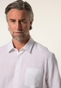 Camicia bianca in lino con colletto strutturato, taschino visibile sul lato sinistro del petto e finitura in tessuto testurizzato.