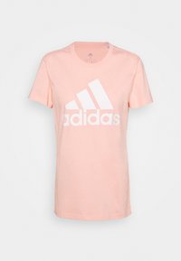 Camiseta de algodón de color rosa claro con mangas cortas y un escote redondo. Presenta un logo blanco de Adidas en la parte frontal en letras gruesas.