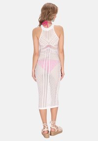 Vit stickad midi-klänning med halterneck, med öppna mönster. Designen har en rosa accent och är kombinerad med kilklackssandaler.