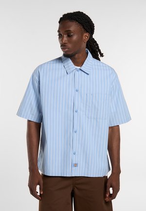 Kortærmet skjorte med knapper i lyseblå med hvide lodrette striber, der har en brystlomme og et diskret logomærke nær kanten.