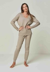 Beige gestricktes Loungewear-Set mit lockerem V-Ausschnitt-Oberteil und enganliegenden Hosen mit gerippter Textur und Bündchen. Material aus Baumwollmischung, lässiges Design.