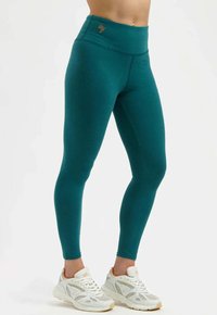Leggings taille haute couleur sarcelle en tissu extensible à texture lisse, avec des coutures latérales et un petit logo sur la ceinture.
