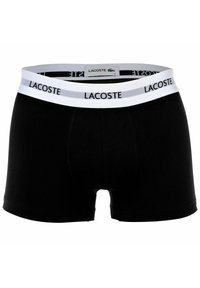 Czarne bawełniane bokserki z białym paskiem, na którym czarną czcionką nadrukowano słowo "LACOSTE". Styl o średnim stanie z dopasowanym krojem.
