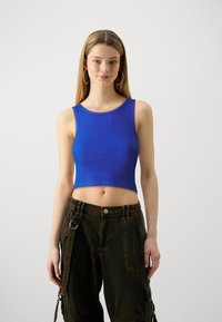 Plavi rebrasti crop top s okruglim izrezom i bez rukava, uparen s tamnim cargo hlačama s džepovima i bočnom trakicom.