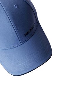 Blauwe stoffen pet met gestikte naden, een gebogen klep en zwarte "HACKETT" branding boven de klep. Soepele textuur, gestructureerd ontwerp.