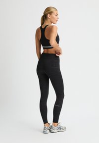 Crop top sportivo nero con design a schiena scoperta, abbinato a leggings a vita alta con un motivo geometrico, e dettagli argentati nelle calzature.