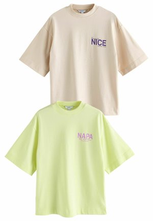 Twee oversized t-shirts staan tentoon: een beige met paarse tekst "NICE" en een lichtgroene met roze tekst "NAPA", beide van katoen.