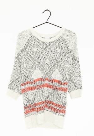 Strickpullover mit geometrischen Mustern in Schwarz und Weiß, mit orangefarbenen horizontalen Streifen. Lange Ärmel und weit geschnittenem Halsauschnitt. Hängt an einem Haken.