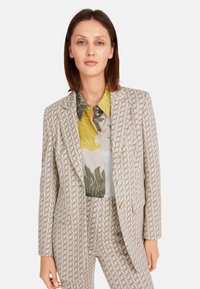 Light beige tailored blazer with geometric pattern, paired with a multicolored floral blouse featuring yellow, green, and gray tones.