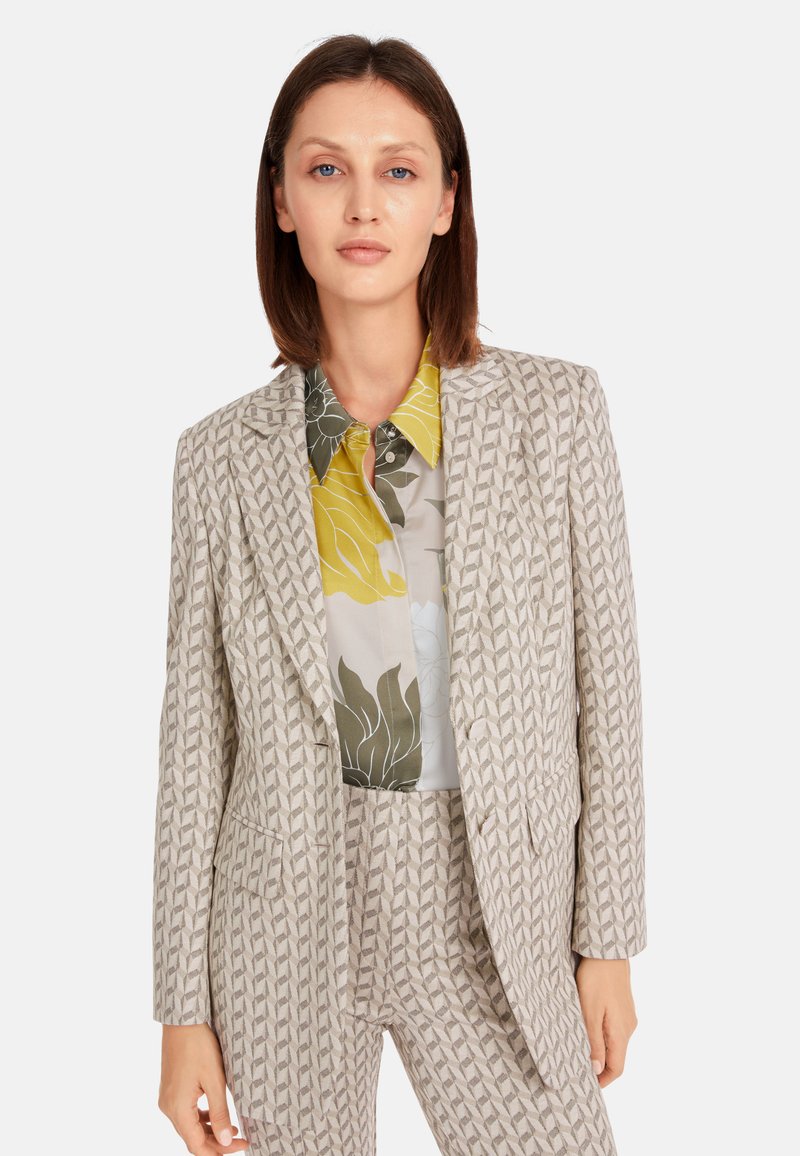 Light beige tailored blazer with geometric pattern, paired with a multicolored floral blouse featuring yellow, green, and gray tones.
