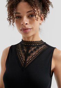 Top negro con un cuello de encaje alto con detalles intrincados, textura acanalada y diseño sin mangas.