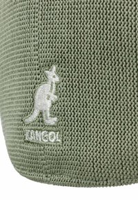 Tessuto verde intrecciato con una finitura texturizzata, caratterizzato da un logo di canguro ricamato in bianco nella parte inferiore. Design semplice e materiale resistente.