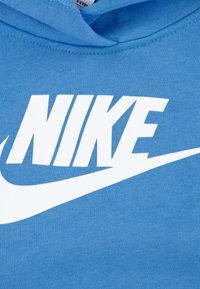 Μπλε φούτερ με μαλακή υφή και μεγάλο λευκό λογότυπο "NIKE", με σχεδιασμό swoosh από κάτω, πάνω σε φόντο υφάσματος.