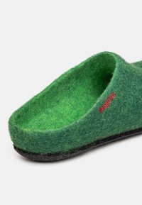 Pantofole verdi in feltro con forma arrotondata, suola in gomma nera e dettaglio del logo rosso. Tessuto morbido e fodera interna accogliente.