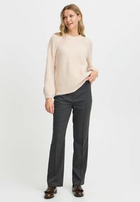 Hellrosa gestrickter Pullover mit gerippter Textur, Rundhals und langen Ärmeln, kombiniert mit grauen, maßgeschneiderten Hosen und braunen Schuhen.