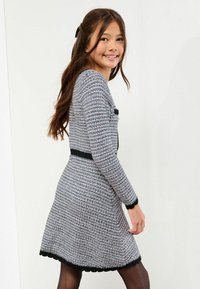 Szara i różowa dzianinowa sukienka w wzory, z falbaniastym czarnym dołem i czarnym pasem w talii, z długimi rękawami i okrągłym dekoltem.