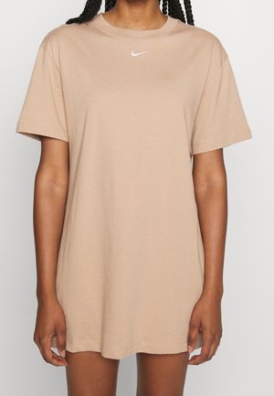 Vrouw draagt een beige oversized Nike T-shirt met korte mouwen en een klein wit logo op de borst.