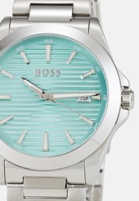 Montre en acier inoxydable argenté avec un cadran rayé bleu clair, des index argentés et un affichage de la date. Résistante à l'eau jusqu'à 50 mètres.