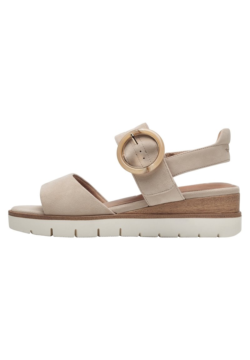 Sandales compensées en daim beige avec un large bout et une sangle de cheville, dotées d'une grande boucle circulaire et d'un accent en bois sur une semelle blanche.