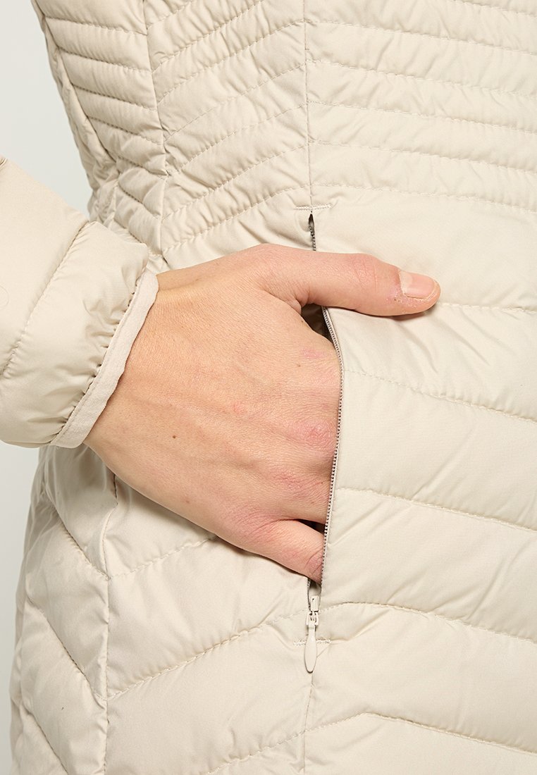 Lichtbeige gewatteerde jas met een ritszak. De stof is glad, met diagonale stiksels en een elastische manchett bij de pols.