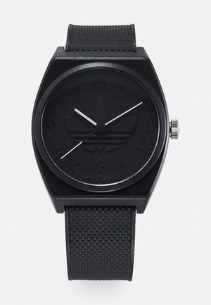 Montre analogique noire avec un boîtier carré, un bracelet texturé noir et un logo en relief sur une lunette mate. Les aiguilles des heures et des minutes blanches contrastent avec le cadran.