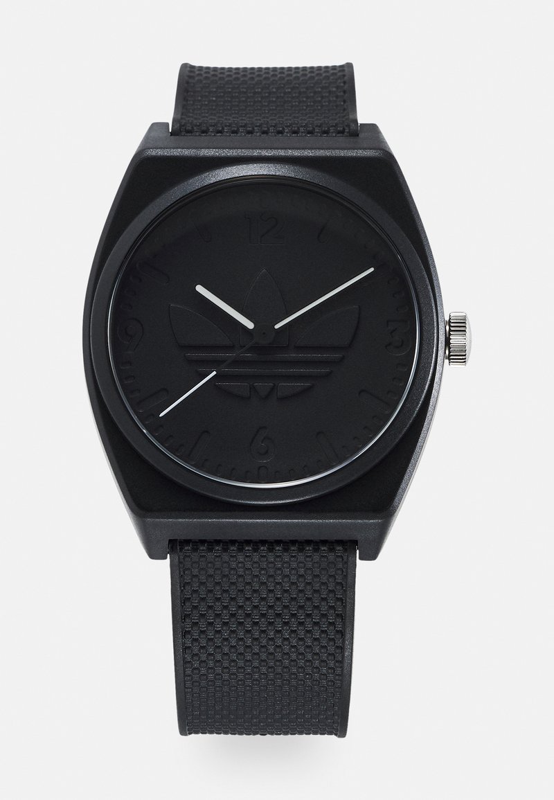 Montre analogique noire avec un boîtier carré, un bracelet texturé noir et un logo en relief sur une lunette mate. Les aiguilles des heures et des minutes blanches contrastent avec le cadran.