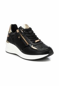 Zapatilla negra con cuero perforado, detalles en dorado y un cierre lateral. Cuenta con una suela de cuña blanca y cordones negros para un ajuste seguro.