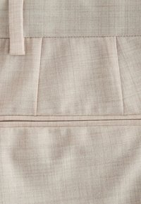 Tissu en lin beige clair avec une ceinture, une boucle de ceinture et des détails de couture plissée sur un vêtement.