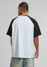 Raglan-sleeve T-shirt in black and white cotton, featuring a relaxed fit and smooth texture, with a plain design and no visible patterns.