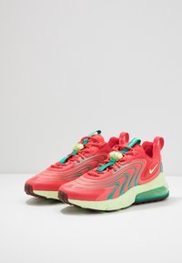 Klart röda och teal atletiska sneakers med gröna snörlås, ljusgröna sulor och luftkuddar i klacken på en vit yta med en enkel bakgrund.