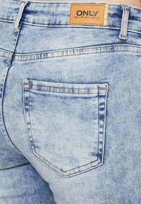Light blue denim jeans featuring a back pocket and a leather label with "ONLY" logo. Distressed texture with contrasting stitching details.