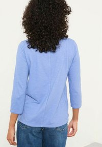 Light blue long-sleeve shirt with a smooth texture, a round neck, and a back seam detail, paired with denim pants.