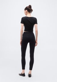 Μαύρο κοντό t-shirt και κολάν ψηλόμεσο, και τα δύο από ελαστικό ύφασμα, με ομαλή υφή και εφαρμοστή σχεδίαση. Μαύρα επίπεδα παπούτσια.